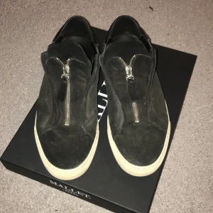 Svarta sneakers från Arigato  - Snygga svarta sneakers från Arigato med dragkedja framtill. Skorna har en stilren design med en vit sula som kontrasterar mot det svarta mockamaterialet. Perfekta för en casual look. (Säljs inte mer)