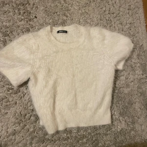 Vit stickad kortärmad tröja från Gina Tricot - Mysig vit stickad tröja från Gina Tricot med korta ärmar. Perfekt för lager-på-lager eller sommarens svalare dagar. Enkel och stilren design som passar till det mesta.