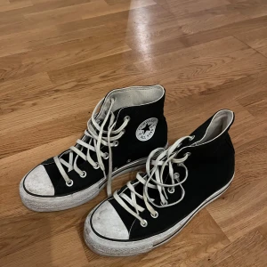 Svarta Converse All Star sneakers - Klassiska svarta Converse All Star sneakers med hög modell och vita snören. Skorna har den ikoniska logotypen på sidan och en vit sula. Perfekta för en avslappnad stil.