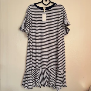 Randig klänning från H&M - Säljer en randig klänning från H&M i marinblått och vitt. Klänningen har korta ärmar och en volangdetalj vid fållen. Perfekt för en avslappnad stil.