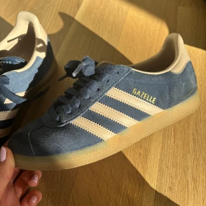 Blå Adidas Gazelle sneakers - Snygga blå Adidas Gazelle sneakers med beiga detaljer. I mycket bra skick då de ej är använda mycket. I storlek 37 1/3.