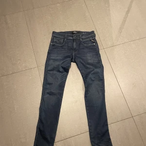 Mörkblå Replay jeans - Snygga mörkblå jeans från Replay i modellen Anbass. De har en klassisk femficksdesign med dragkedja och knapp framtill. Perfekta för en stilren look. Helt nyskick och aldrig burits. Snygg tvätt och flex