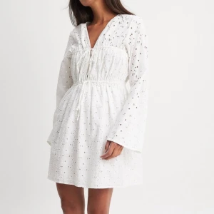 Vit klänning  - Söt vit klänning från NA-KD med broderade detaljer och knytning framtill. Perfekt studentklänning eller till midsommar! Aldrig använd. Storlek Xs 