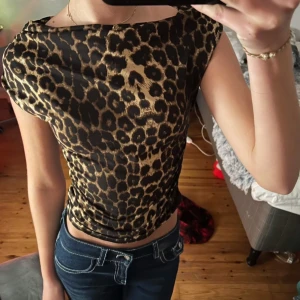 Leopardmönstrad topp - Säljer en snygg leopardmönstrad offshoulder topp med rynkade detaljer. Toppen har en ganska tajt passform och är perfekt för att ge en cool look. Materialet är mjukt och stretchigt, vilket gör den bekväm att bära.
