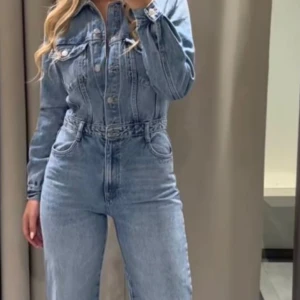 Blå jeans jumpsuit från Zara - Snygg blå jeans jumpsuit med långa ärmar och knappar framtill. Den har en klassisk krage och flera fickor för en cool look. Ej använd och lappen sitter kvar. Nypris 559kr