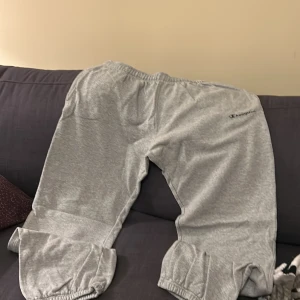 Grå mjukisbyxor från Champion - Säljer ett par grå mjukisbyxor från Champion. De har en elastisk midja och muddar vid bensluten för extra komfort. Perfekta för en avslappnad stil.