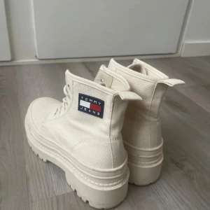 Vita boots från Tommy Jeans - Snygga vita boots från Tommy Jeans i canvasmaterial. De har en robust sula och snörning framtill. Perfekta för en stilren look med en touch av streetwear. Märkeslogga på sidan ger en extra detalj.
