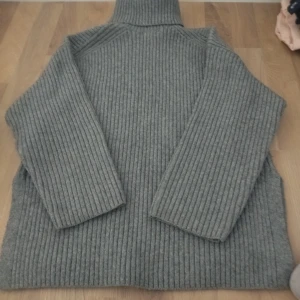 Grå ribbad polotröja - Säljer en stilren grå polotröja med ribbad design. Tröjan har långa ärmar och en hög krage som ger extra värme. Perfekt för kyliga dagar.