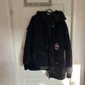 Svart parkajacka från Canada Goose - Säljer en svart parkajacka från Canada Goose, perfekt för kalla dagar. Jackan har långa ärmar och flera praktiska fickor. Den har en ikonisk logga på bröstet. Perfekt för vinterns äventyr! ❄️saknar päls. Lite små smuts här och där, men annars varm och go.
