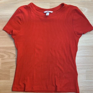 Röd ribbad topp från H&M - Säljer en snygg röd ribbad topp från H&M. Den har en enkel design med korta ärmar och rund halsringning. Perfekt för en casual look eller att styla upp med accessoarer. Passar bra till både jeans och kjol. 🌟