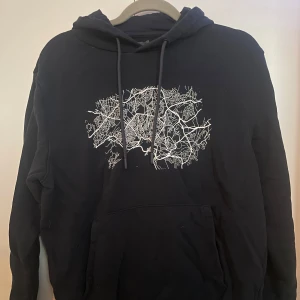 Mörkblå hoodie från Dressmann - Säljer en mörkblå hoodie från Dressmann med ett unikt vitt kartmönster på framsidan. Tröjan är tillverkad i en mjuk bomullsblandning och har en klassisk känguruficka framtill. Perfekt för en avslappnad stil. Hund finns i hemmet.
