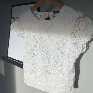 Vit spetsblus från Gina Tricot - Säljer en söt vit spetsblus från Gina Tricot. Blusen har korta ärmar och en öppen rygg med knappar. 🌸