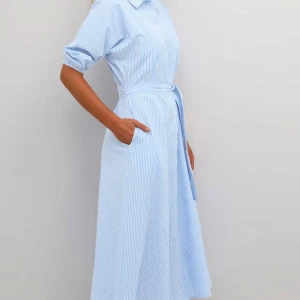 Blå- och vitrandig klänning med knytband - Snygg blå- och vitrandig klänning med knytband i midjan och trekvartsärmar. Perfekt för en stilren look. Klänningen har en klassisk krage och knappar framtill. Ny med prislappen på . Från danska kaffe