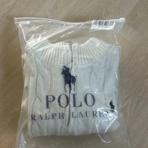 Vit stickad tröja från Ralph Lauren - Säljer en vit stickad tröja från Ralph Lauren med kabelstickat mönster. Tröjan har en dragkedja vid halsen och långa ärmar. Perfekt för kyligare dagar. Använt den ett få tal gånger. Finns en liten streckning av ullet på vänster arm. Kan skicka bild i privat, har några frågor hör av