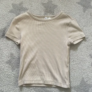 Beige ribbad topp från Hm - Säljer en stilren beige ribbad topp från Divided. Den har en enkel design med korta ärmar och rund halsringning. Perfekt för en sommardag! Aldrig använd!