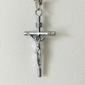 Silverfärgat korshalsband med Jesusfigur - Stilrent silverfärgat halsband med ett korshänge som har en detaljerad Jesusfigur. Hänget är dekorerat med små stenar som ger en extra glans. Perfekt för att bära till både vardag och speciella tillfällen.