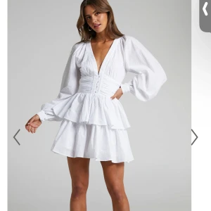 Vit klänning med volangdetaljer - Säljer en superfin vit klänning med volangdetaljer och v-ringning från Showpo. Klänningen har långa ärmar och en kort längd, perfekt för studenten! Helt ny och prislappen är på!