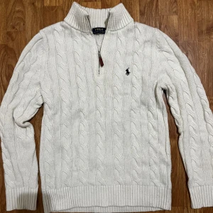 Stickad halfzip från Ralph Lauren - Säljer en stilren vaniljig färg stickad tröja från Ralph Lauren med kabelstickat mönster och en broderad logga på bröstet.  Halfzippen är i top kvalitè användes ungefär en hel vecka totalt men inga märken är synliga. För mer information hör gärna av er✅