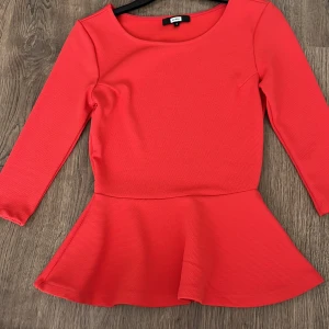 Röd topp med volangdetalj - Snygg röd topp från bikbok med volangdetalj i nederkant. Toppen har trekvartsärmar och en rund halsringning. Perfekt för att ge en färgklick till din outfit!  Kunden står för frakten/ alternativt mötas upp i Norrköping!