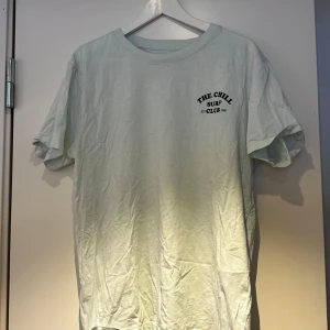 Ljusgrön t-shirt med tryck - Säljer en ljusgrön t-shirt med trycket 'The Chill Surf Club' på bröstet. T-shirten har korta ärmar och en rund halsringning. Perfekt för en avslappnad stil.