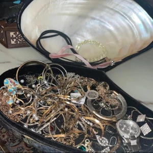 Smyckessamling med klocka och armband mm - En samling av olika smycken inklusive en klocka med glittrig urtavla och ett armband från Guess. Det finns flera halsband och armband i både guld- och silverfärger, samt smycken med pärlor och färgade stenar.