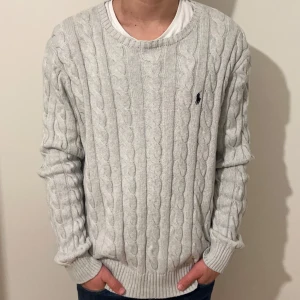 Grå Kabelstickad Ralph Lauren Tröja - En grå Kabelstickad Ralph Lauren tröja Storlek M, sitter lite oversized // Fungerande QR kod // Har en pytteliten fläck som t.om är svår att få på bild för att den inte syns alls men annars är den i toppskick