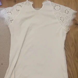 Vit blus med spetsdetaljer - Säljer en söt vit blus med vackra spetsdetaljer på ärmarna. Vet inte riktigt vart den är köpt men skulle säga att de passar Xs- M.  
