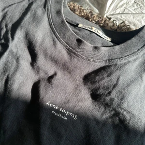 Svart t-shirt från Acne Studios - Säljer en stilren svart t-shirt från Acne Studios med tryck på bröstet. Tillverkad i mjuk bomull för en bekväm känsla. Perfekt för en minimalistisk look. Storlek xxs men oversized