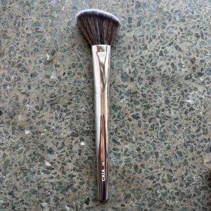 Sminkborste från Caia - Sminkborste från Caia med silverfärgat handtag och mjuk borst. Perfekt för att applicera puder, bronzer eller blush. Aldirg använd