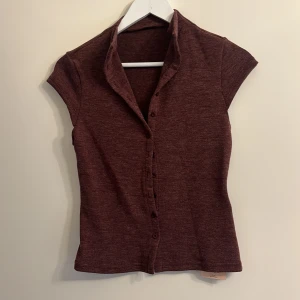 Vinröd kortärmad topp med knappar - Snygg vinröd topp med korta ärmar och knappar framtill. Perfekt för en stilren look.
