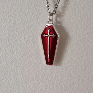 Rött kistformat halsband med kors - Unikt halsband med en röd kistformad berlock och ett silverfärgat kors i mitten. Kedjan är i silverfärg och berlocken har en blank yta som ger en cool kontrast. Perfekt för att ge din outfit en edgy touch.