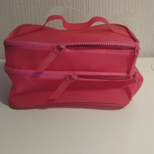 Rosa necessär med dragkedja - Säljer en praktisk rosa necessär 22x14x12 cm  med två dragkedjor och ett handtag på toppen. Perfekt för att organisera dina saker. Den har en enkel och stilren design.