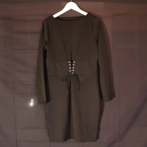 Svart klänning med snörning - Snygg svart klänning med långärmad design och cool snörning i midjan. Perfekt för en stilren look. Klänningen har en enkel och elegant form som passar till många tillfällen.