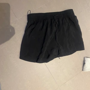 Svarta shorts med snörning - Snygga svarta shorts med elastisk midja och snörning för justerbar passform. Perfekta för en avslappnad stil under varma dagar. Enkla att matcha med olika toppar.