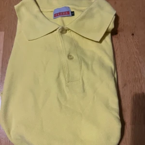 Gul pikétröja från Prada - Snygg gul pikétröja från Prada med klassisk krage och knappar framtill. Perfekt för en stilren och avslappnad look. Tröjan har korta ärmar och är tillverkad i ett bekvämt material.