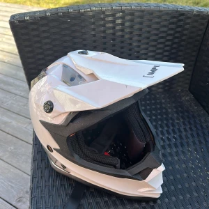 Vit cross hjälm från Impulse - Säljer en vit hjälm från Impulse med svart inredning och justerbar skärm. Perfekt för motorcykelentusiaster som söker stil och säkerhet. Märkt med ECE R 22.05 för säkerhetsstandard. Skicket är bra några skråmor på insidan men funkar perfekt för en person som precis tagit sitt AM kort. 