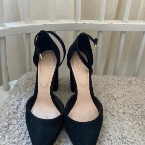 Svarta pumps från Aldo - Snygga svarta pumps från Aldo med spetsig tå och klack. Skorna har en elegant design med en rem runt ankeln för extra stil och komfort. Perfekta för att lyfta din outfit till nästa nivå. Pris kan diskuteras, skriv om ni är intresserade 💕💕