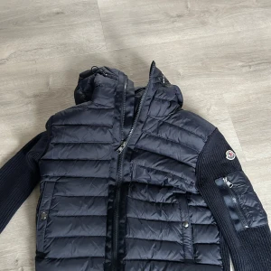 Moncler cardigan - Snygg mörkblå cardigan från Moncler med dragkedja och huva. Jackan har långa ärmar och en quiltad design. Perfekt för kyligare dagar.
