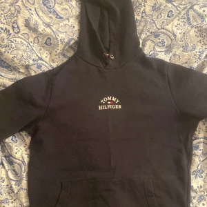 Mörk blå hoodie från Tommy Hilfiger - Säljer en mörkblå hoodie från Tommy Hilfiger med klassisk logga på bröstet. Den har en bekväm passform och en praktisk magficka. Perfekt för en avslappnad stil.