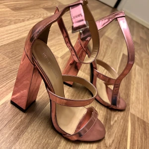 Rosa klackskor från Public Desire - Snygga rosa klackskor med öppen tå och bred klack. Skorna har en glansig finish och justerbara remmar runt ankeln för en perfekt passform. Perfekta för att ge en färgklick till din outfit!