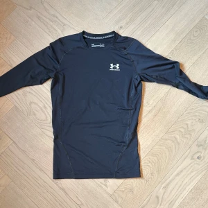 Svart compression shirt från Under Armor - Säljer en svart långärmad tröja från Under Armour. Perfekt för träning med sin tighta passform och bekväma material. Tröjan har en diskret logga på bröstet och ryggen.