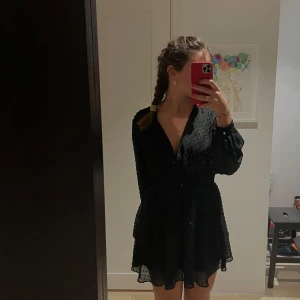 Svart klänning med v ringning - Snygg svart klänning med diskret prickigt mönster och v-ringad design. Klänningen har långa ärmar och en smickrande passform med markerad midja. Perfekt för en stilren look.  Passar även S