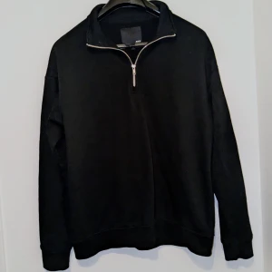 Svart tröja med dragkedja från 157 - Säljer en stilren svart tröja från 157 med en praktisk dragkedja vid halsen. Perfekt för en avslappnad look. Tröjan har långa ärmar och en bekväm passform.