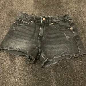 Svarta jeansshorts från Zara - Snygga svarta jeansshorts från Zara med fransiga kanter och slitna detaljer. Perfekta för en avslappnad stil. De har en klassisk femficksdesign och knappgylf.