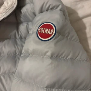 Ljusgrå/ljusblå dunjacka från Colmar - Säljer en jättefin ljusgrå tunnare dunjacka från Colmar. Jackan har en dragkedja framtill och är långärmad. Bra skick!!