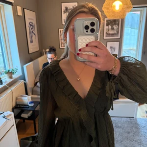 Mörkgrön blus med volangdetaljer - Säljer en elegant mörkgrön blus med volangdetaljer och v-ringning. Blusen har långa ärmar och en omlott-design som ger en smickrande passform. Perfekt för höst och vinter!