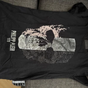 Svart t-shirt med dödskalle från Philipp Plein - Snygg svart t-shirt från Philipp Plein med ett stort dödskalletryck i silver på framsidan. T-shirten har korta ärmar och en rund halsringning. Perfekt för en cool och edgy stil.