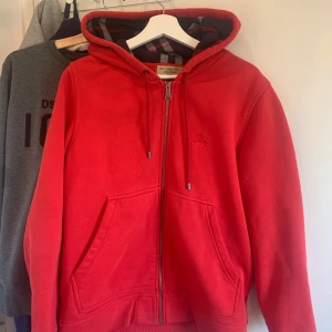 Röd burberry hoodie - Säljer en snygg röd hoodie från Burberry, tröjan är något äldre men fortfarande som ny skick.    Pris kan diskuteras och byten tas också