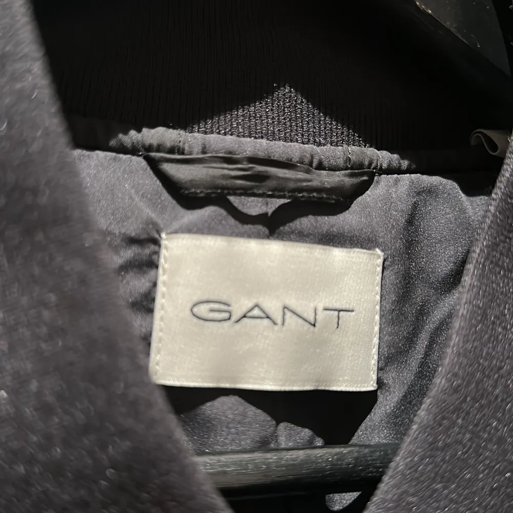 Snygg svart quiltad jacka från GANT med broderad logga på bröstet och ryggen. Jackan har långa ärmar och stängs med knappar framtill. Perfekt för en stilren look.. Takit.