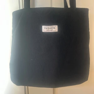 Svart axelväska från SHEIN - Snygg svart axelväska med en enkel design. Väskan har två handtag och en liten etikett med texten 'Fashion Instinct” på framsidan. Perfekt för att bära med sig det nödvändigaste.